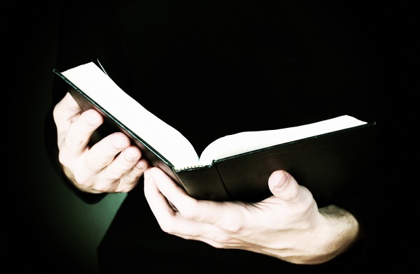 Hands holding open russian bible on black background